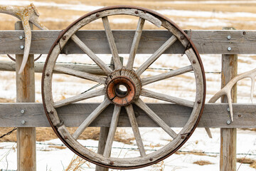 Fototapeta na wymiar Old and weather worn wagon wheel adorns a fence on a ranch in the Grasslands region of Alberta