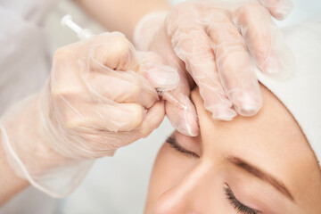 Obraz na płótnie Canvas Forehead injection at spa salon. Doctor hands. Closeup. High quality. Pretty female patient. Beauty treatment. Healthy skin procedure. Young woman face. Light background. Plasmolifting rejuvenation