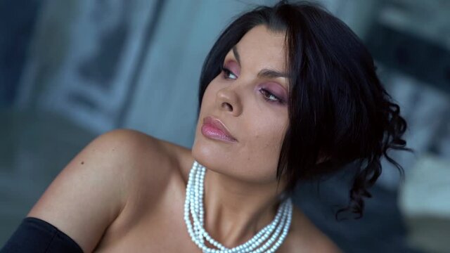 luxury pretty woman with pearls jewelry on neck is posing in interior, closeup portrait