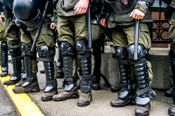 Legs of a policemen in protective ammunition and a green uniform. Knee pads, helmets, batons, boots.