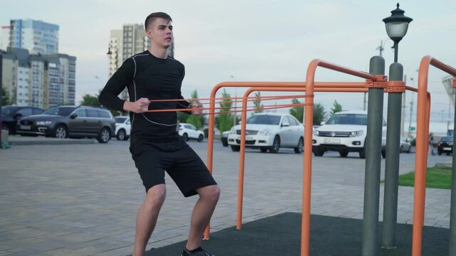 Young muscular man doing exercises with elastic band outdoors. Workout