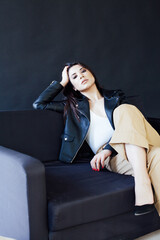 Beautiful fashionable brunette woman in a leather jacket on an office sofa