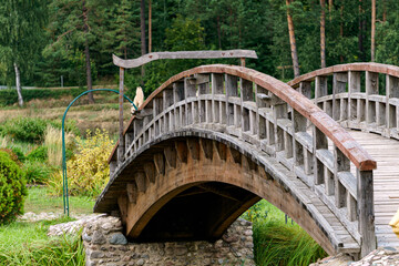 A curved wooden footbridge over a small canal in a summer landscape.