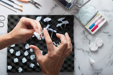 Artist's hands in process of creating hydrangea flowers from polymer clay at the work table