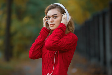 Happy woman in red pullover listening music through headphones in the autumn park