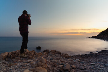 Long exposure back view of a photographer taking pictures at Cala Regina's beach at sunset