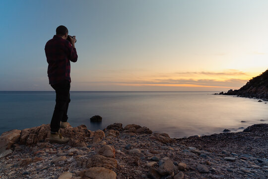 Long exposure back view of a photographer taking pictures at Cala Regina's beach at sunset