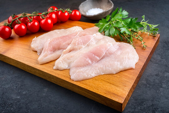 Raw traditional chicken escalope with tomatoes and herbs offered as close-up on a modern design wooden board with copy space