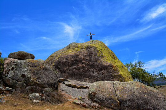 Persona hombre de pie con los brazos extendidos sobre la sima de roca gigante en el parque natural "Las Piedrotas", con el cielo azul y escasa nubes