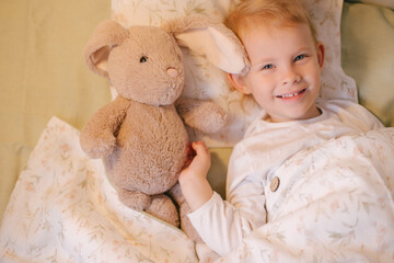 Cute child little girl posing in bed with white linen hugging her soft toy.