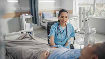 Hospital Ward: Friendly Chinese Head Nurse / Doctor Sitting Beside Bedridden Recovering Male...