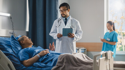 Hospital Ward: Friendly Chinese Doctor Talks to Handsome Male Patient Resting in Bed, Uses Tablet Computer, Explains Test Results. Physician Talks to Man Recovering after Successful Surgery