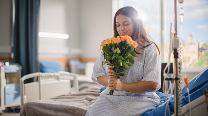 Hospital Ward: Happy Smiling Latin Female Patient is Sitting on Bed and Holding Received Yellow Flowers with Good Analysis Results. Her Treatment is Already Done. Woman Recovering after Surgery.