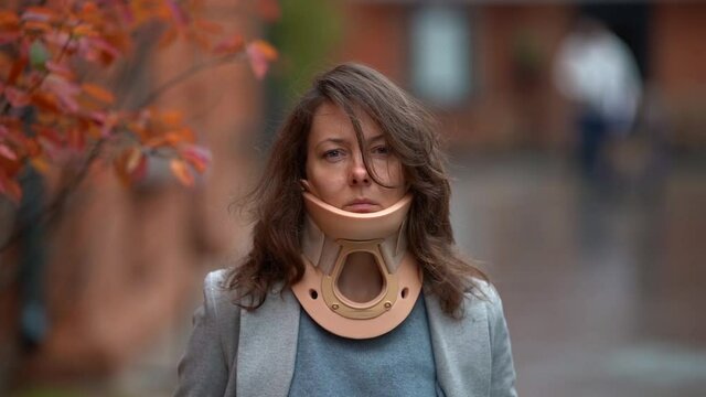 portrait of sad woman with injury of spine or neck outdoors, lady is wearing cervical collar for curing ache