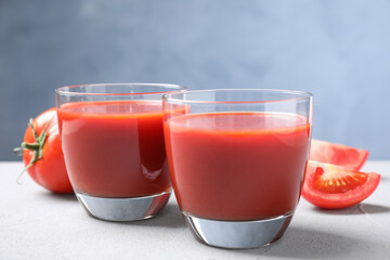Delicious fresh tomato juice on light grey table against light blue background, closeup