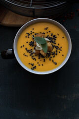Closeup view of a delicious carrot and pumpkin cream soup in a bowl with some leaves of sage at the top. A copy space is at the bottom.