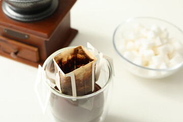 Glass with drip coffee bag on white table, closeup