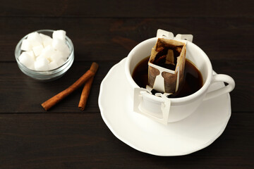 Cup with drip coffee bag, sugar and cinnamon on brown wooden table
