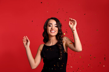 Beautiful young woman wearing elegant dress and confetti on red background. Christmas party