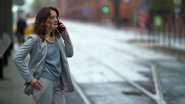 woman with cervical collar is standing on city street and talking by mobile phone, curing and prevention