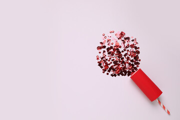 Shiny red confetti bursting out of party cracker on light background, top view. Space for text
