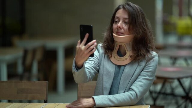 sick woman with neck ache after injury is wearing cervical collar for fixing and curing spine, chatting online in cafe