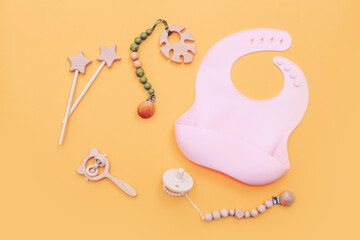 Pink silicone bib and other baby accessories on yellow background, top view.