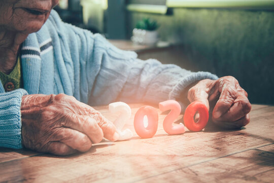 Old Person Hands Holding Number 2020 On Wood Table.