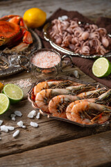 Dishes with assorted seafood. Cooked crab with ice-cubes, baby octopuses and tiger shrimps served with lime and seashells on rustic wooden background. Seafood concept. Delicious meal.