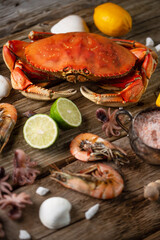 Assorted seafood. Cooked crab with ice-cubes, baby octopuses and tiger shrimps served with lime and seashells on rustic wooden background. Seafood concept. Delicious meal.