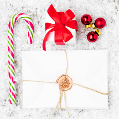 Flat lay of Christmas gift or present with red ribbon, balls, candy stick and envelope with wax stamp. Letter for Santa Claus. 
