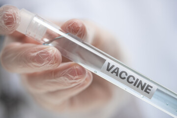 Close-up view of hand in protective gloves holds biological tube with label vaccine. Laboratory...