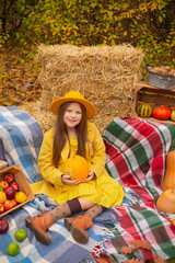 cute beautiful teenage brunette girl in an orange hat, dress and coat next to autumn decorations - pumpkins, apples, blankets, hay. Cosiness