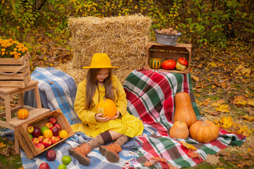 cute beautiful teenage brunette girl in an orange hat, dress and coat next to autumn decorations - pumpkins, apples, blankets, hay. Cosiness