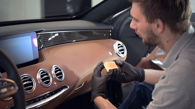 Man applying protection layer of ceraminc coating on a car dashboard with special applicator.