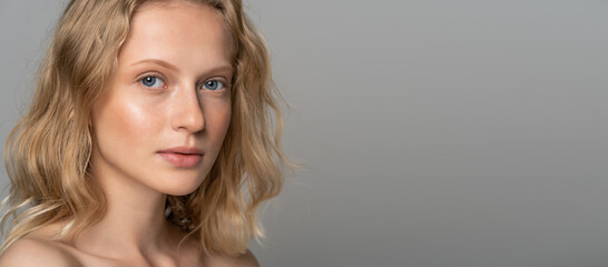 Close up of young woman face with blue eyes, curly natural blonde hair and eyebrows, has no makeup,...