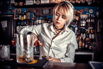 Focused woman bartending makes a cocktail at the bar counter