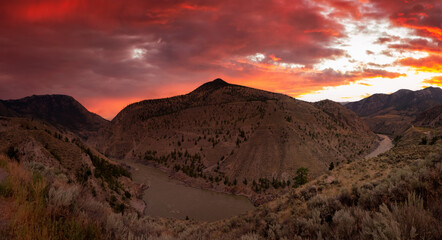 Aerial Panoramic View of Fraser River running in the valley surrounded by Canadian Mountain Landscape. Dramatic colorful sunset sky in summer. Taken near Lillooet, BC, Canada.