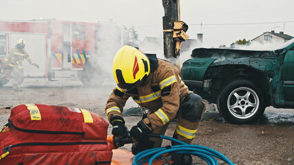 Firefighter preparing the hose wor hidraulic cutter on the car crash scene. High quality photo