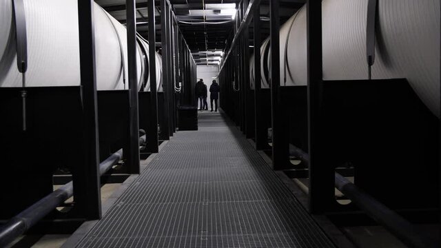 Rear view of three men walking along water treatment tanks at the power plant. Media. Corridor with huge reservoir tanks for water purification, ecology concept.
