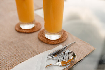 Fork, spoon and knife wrapped in papper napkin on the table near glasses of juice