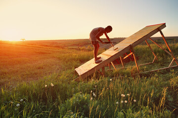 Young Caucasian man paints new mtb gap in the field at sunset. The springboard is designed for...