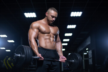 Fototapeta na wymiar Muscular sexy bodybuilder is working out doing weight lifting of the barbell in gym