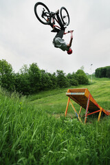 Young Caucasian man jumping on a mountain bike from a springboard in the forest.