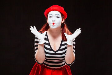 Fototapeta na wymiar Portrait of female mime artist performing, isolated on black background. Woman in striped clothes and red skirt is standing with raised hands amazed. Symbol of wonder, admiration, worship