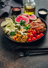 Buddha bowl with brown rice, grilled chicken breast, avocado, tomato, peas, corn, watermelon radish, asparagus