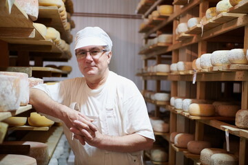 Cheese maker at the storage with shelves full of cow and goat cheese