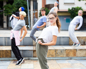 Modern young girl dancing with group of friends on city street. Urban lifestyle. Z generation.