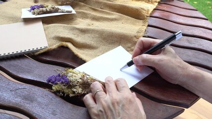 
senior woman writing invitation card made of dry flowers to friend