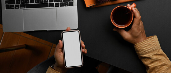Male hand using smartphone and holding coffee cup on worktable
